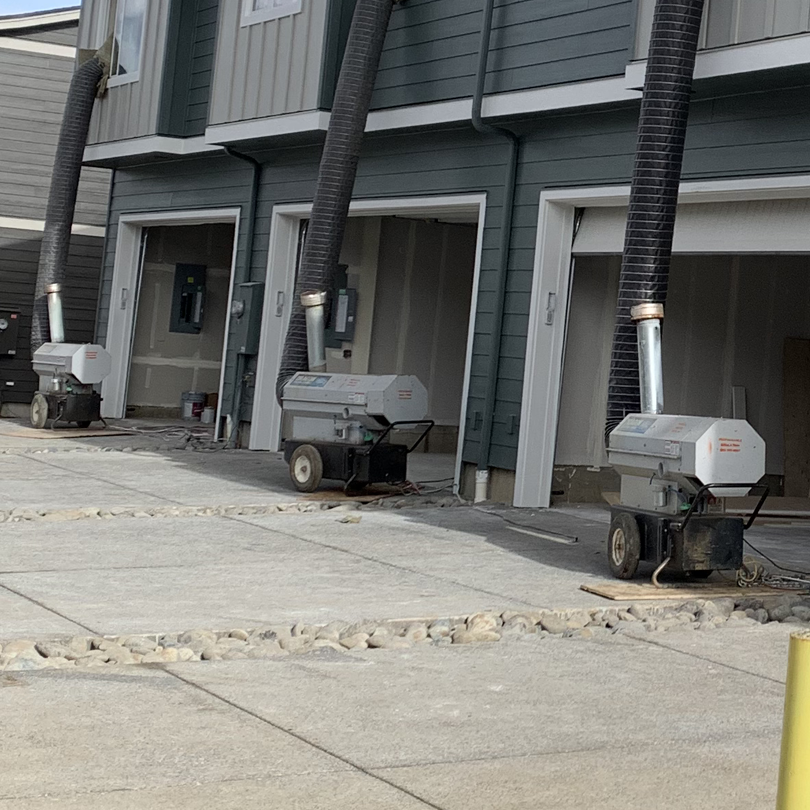 3 dragon heaters with hoses connecting them to the upstairs windows of a multifamily build